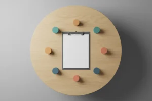 Top-down view of a round table with a blank clipboard at center and four colored tokens arranged around it.