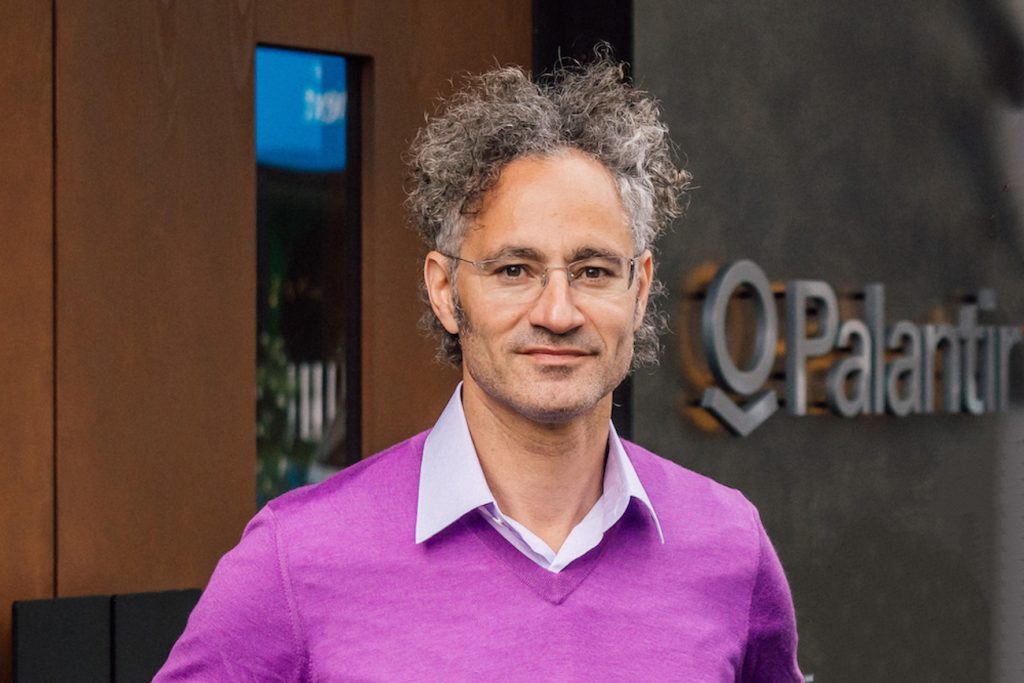 Palantir CEO Alex Karp stands outside a Palantir office in a purple sweater.