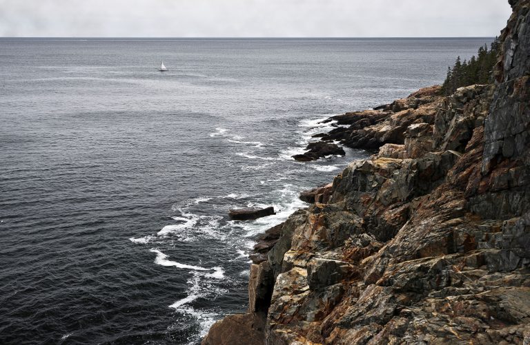Rocky shoreline and a distant sailboat near Bar Harbor, Maine