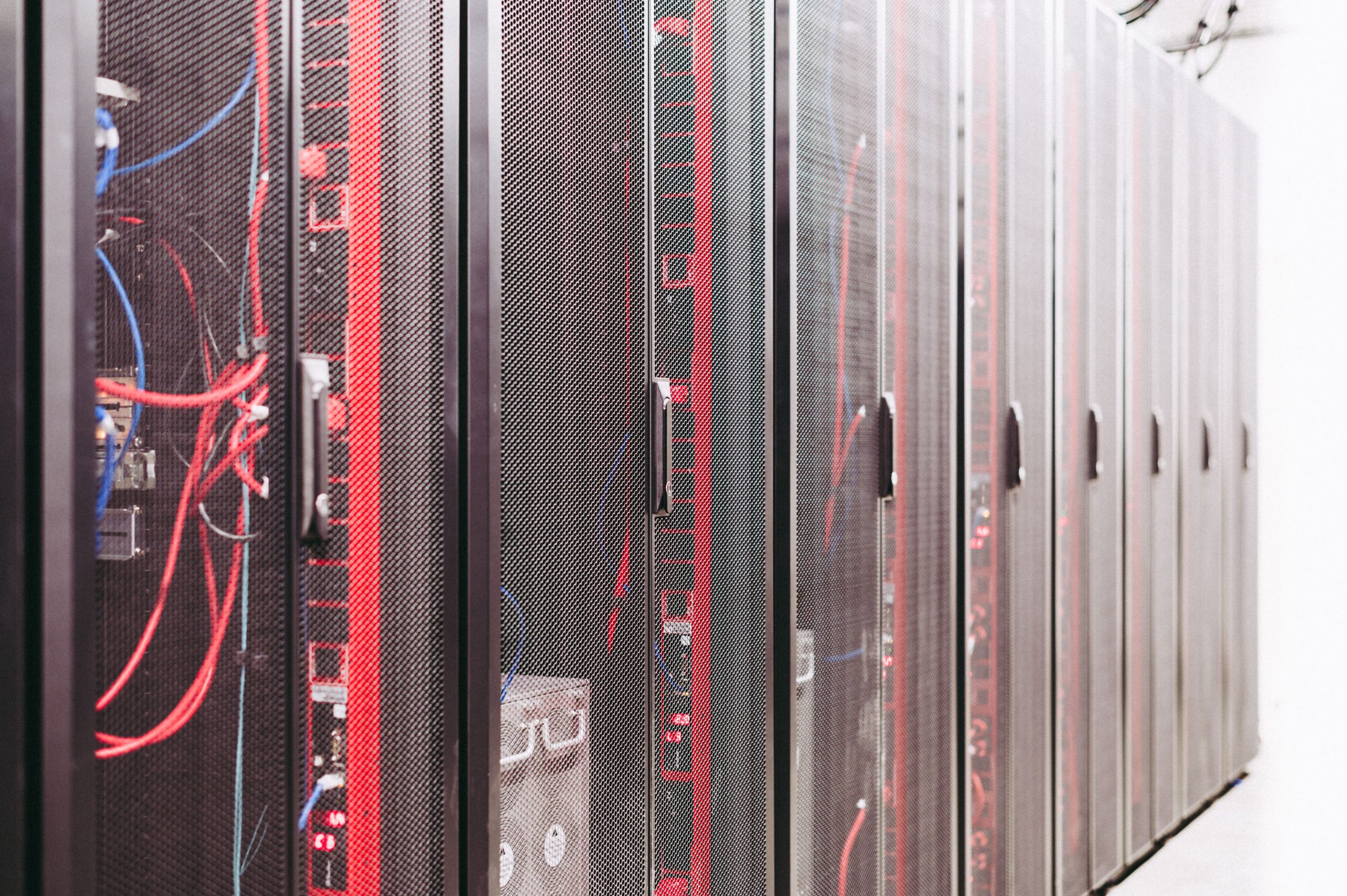 Rows of enclosed server cabinets with red and blue cabling in a data center