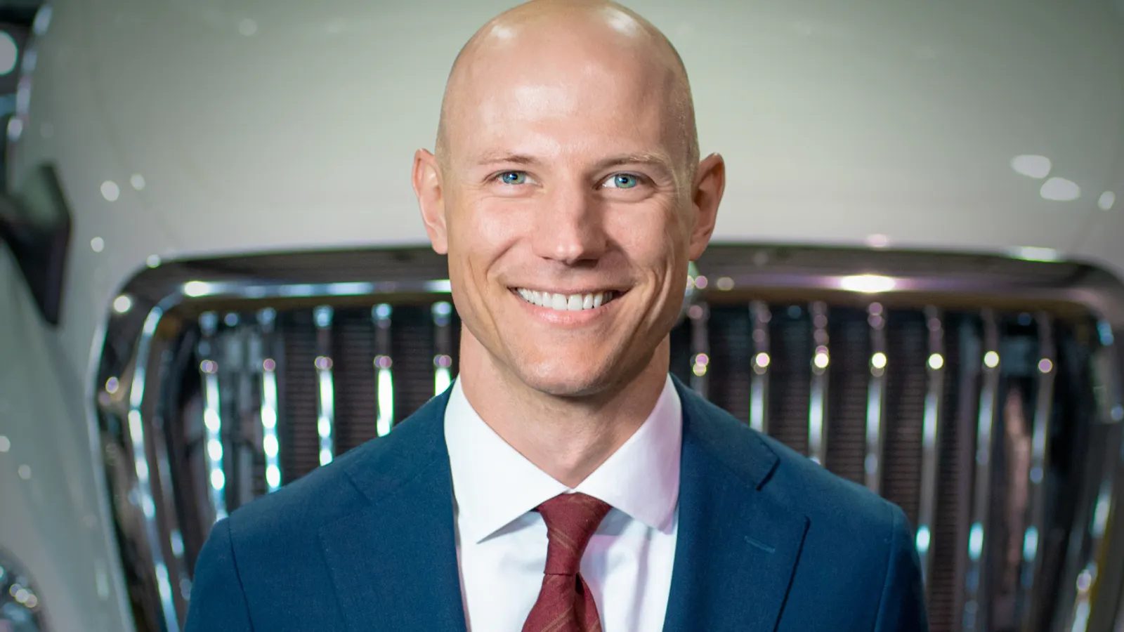 Mark Colson wearing a suit and tie in front of a truck grille