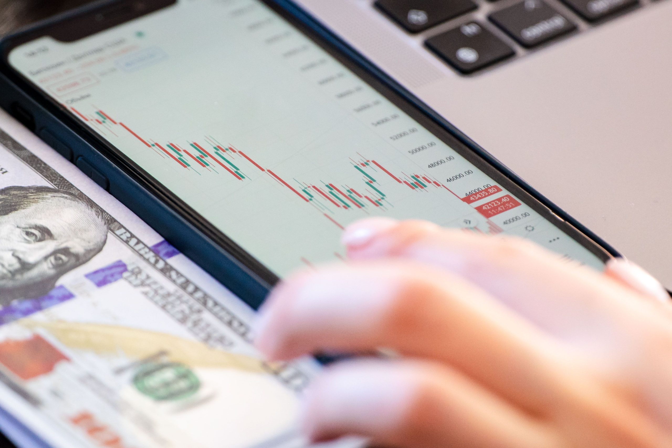 Investor reviews a market chart on a phone beside a dollar bill