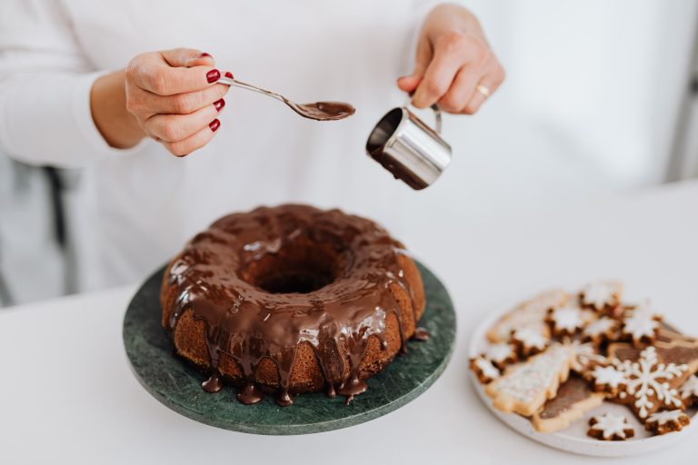 Hands pour chocolate icing over a bundt cake