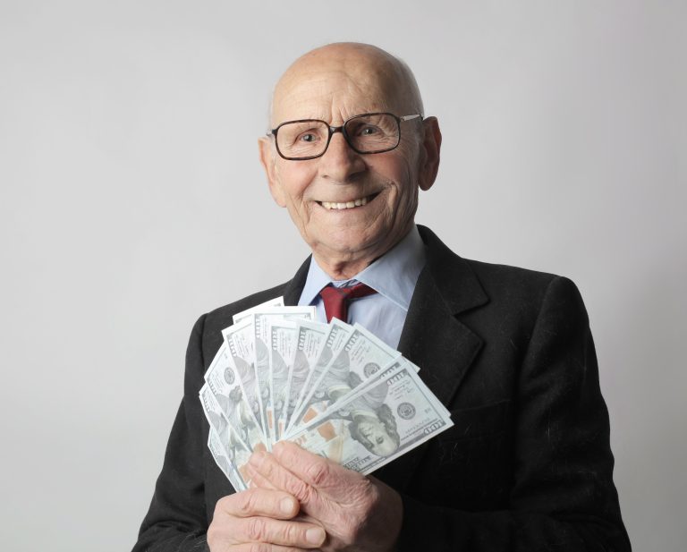 Senior man in a suit with glasses holding US dollars, symbolizing wealth and savings
