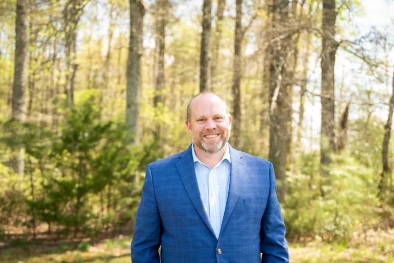 Middle-aged man smiling in outdoor forest with a suit jacket, trees in background