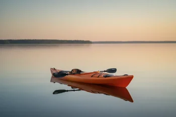 Lone saffron kayak with paddle on a calm misty lake at dawn, soft neutral background.