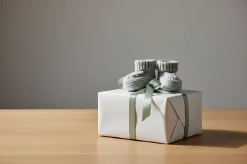 Wrapped gift box with ribbon and tiny baby booties on a clean desk, symbolizing a warm welcome back from parental leave.