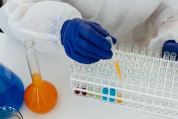 Gloved researcher pipettes colorful samples into a rack of laboratory tubes